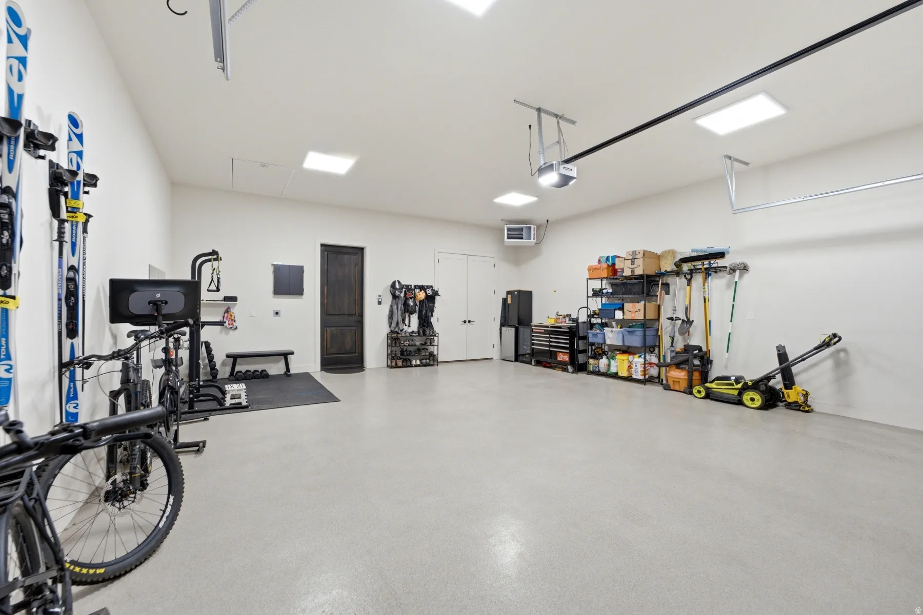 Spacious garage featuring a light-colored floor, multiple overhead light fixtures, and a dark wood-finish door