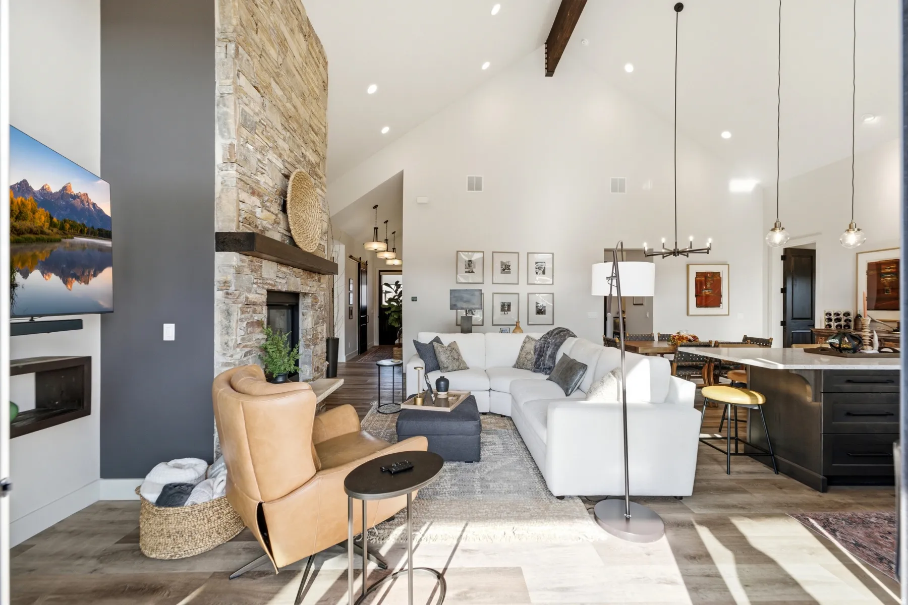 Vaulted ceilings, a stone-finish fireplace with a wood mantel, wood-finish flooring, and recessed lighting illuminate the open-concept living space