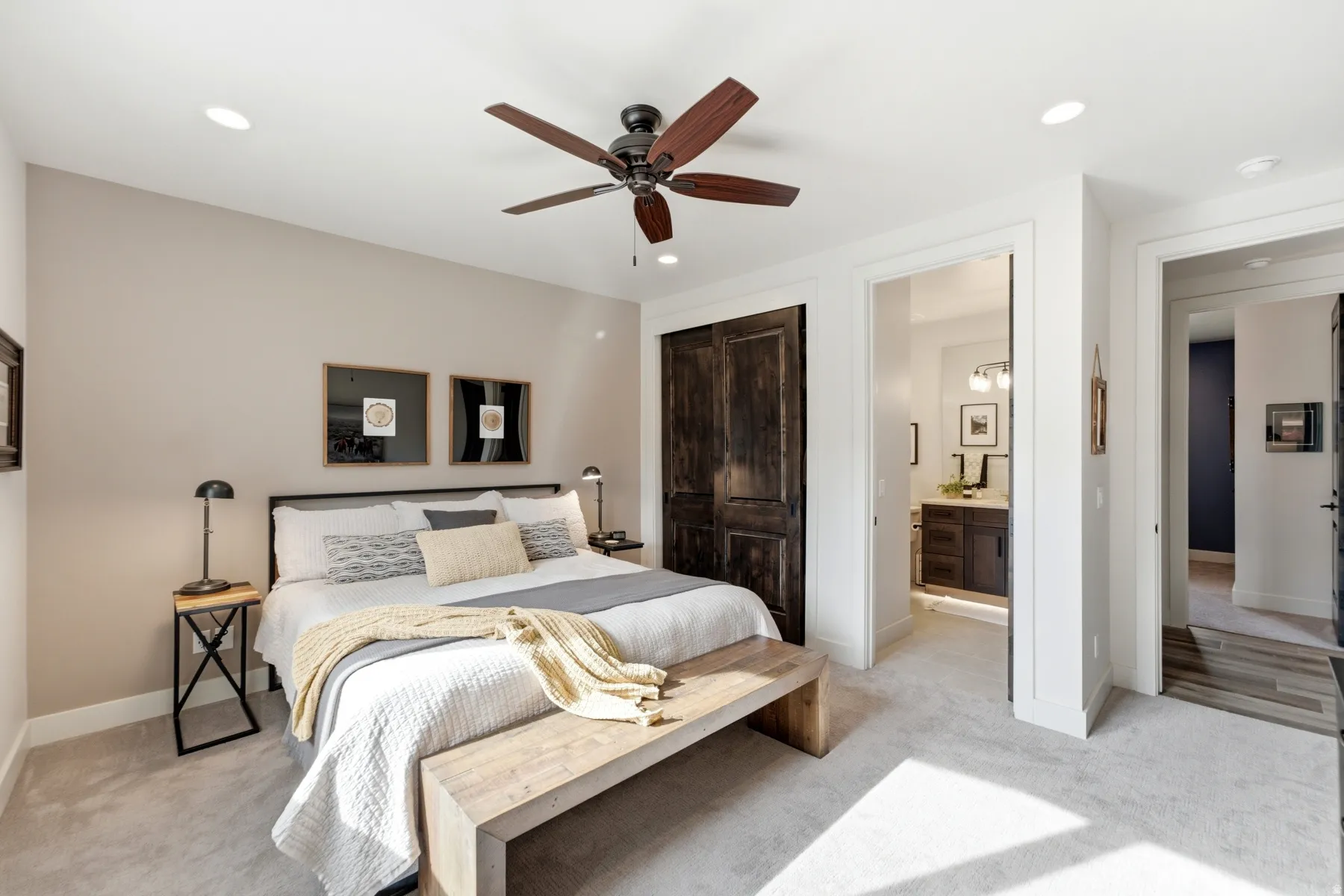 Vaulted ceiling with recessed lighting and ceiling fan, dark wood-finish barn doors, light-toned carpet flooring, and a bathroom featuring a dark wood-finish vanity