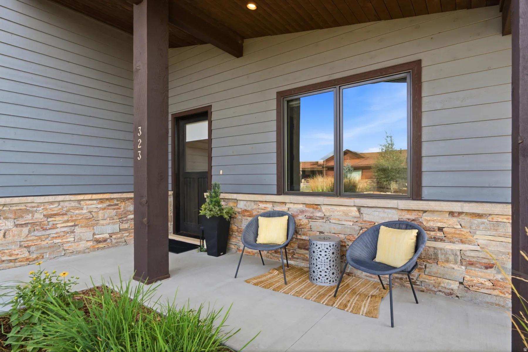 Covered concrete front porch featuring a wood-finish ceiling, stone veneer accents, gray horizontal siding, and a dark entry door with frosted glass
