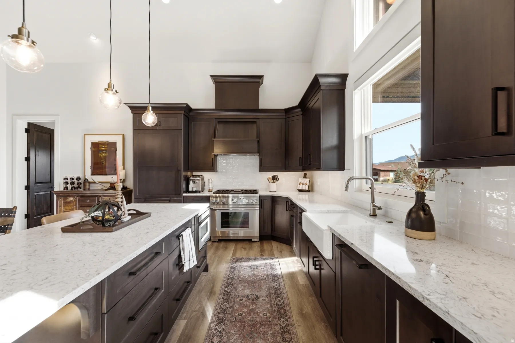 Kitchen with dark wood cabinetry, light-colored countertops, a white farmhouse sink, and stainless steel appliances