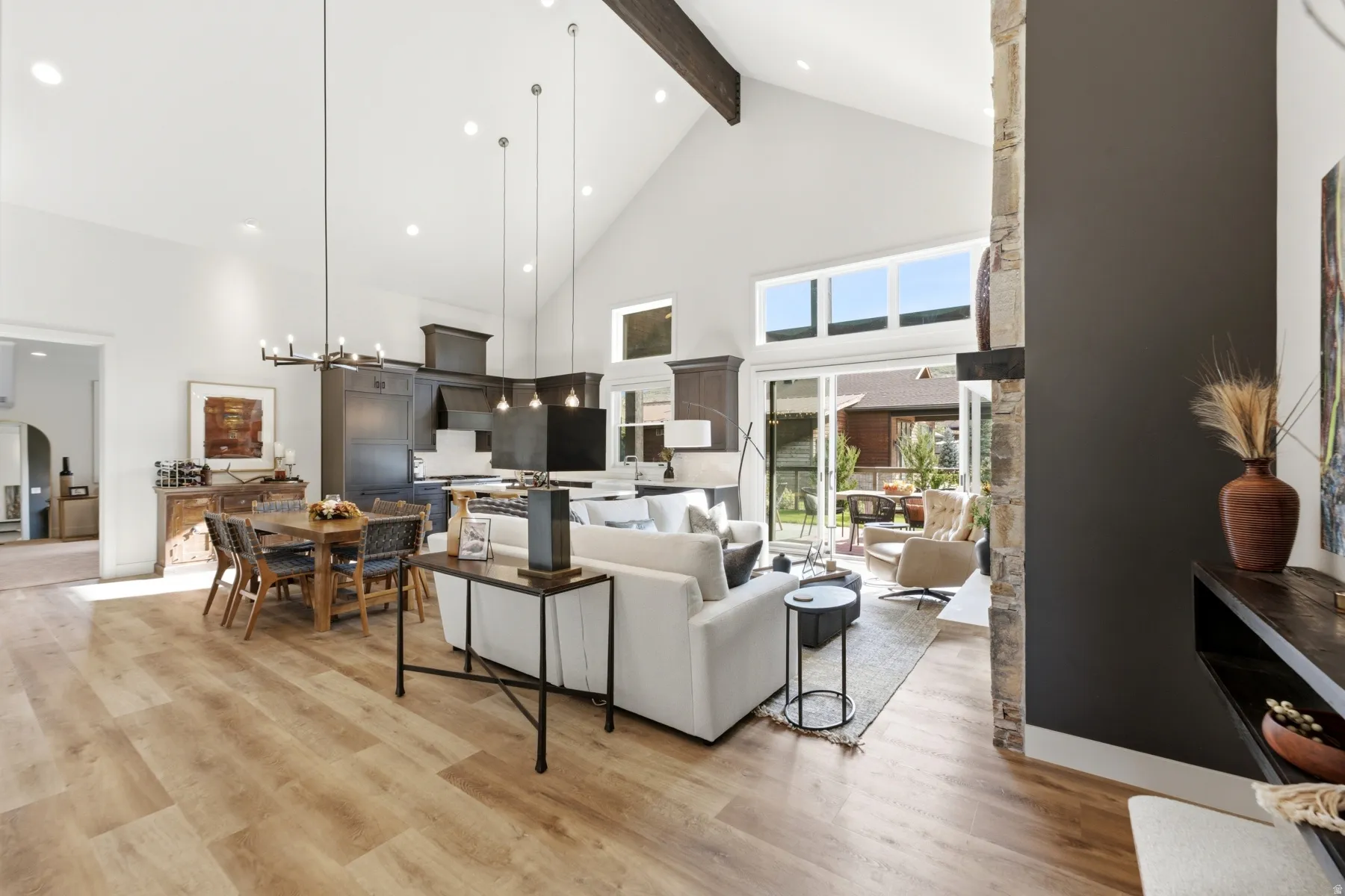 Vaulted ceilings with exposed beam, wood-finish flooring, sliding glass doors to outdoor space, dark wood cabinetry, and a stone accent wall