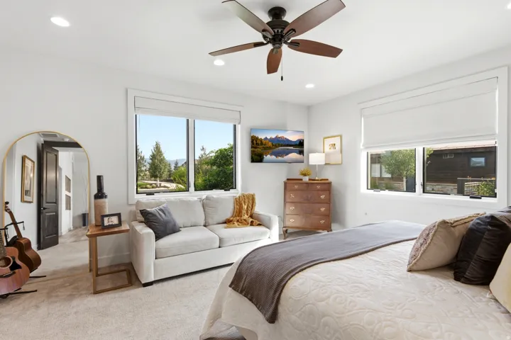 Recessed ceiling lighting, wood-finish ceiling fan, expansive windows, light-toned carpeting, and a dark-paneled interior door