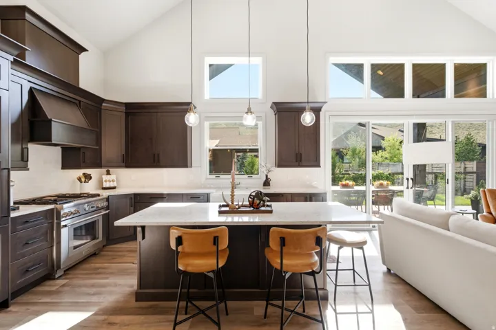 Vaulted ceiling with abundant natural light, dark wood-finish cabinetry, stainless steel range, light-toned countertops, and wood-finish flooring
