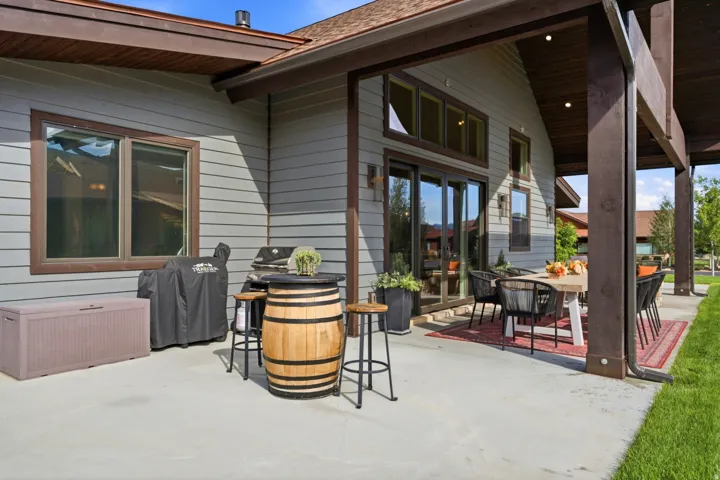 Expansive concrete patio with a covered outdoor dining area, wood-clad soffits, and exterior wall sconces