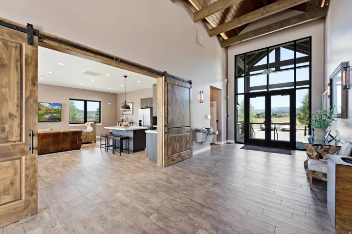 Grand entryway featuring a vaulted wood-beam ceiling, full-height glass-paneled doors, and wood-finish flooring