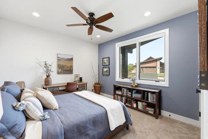 Recessed ceiling lighting, wood-finish ceiling fan, expansive window, light-toned carpeting, and a built-in desk area