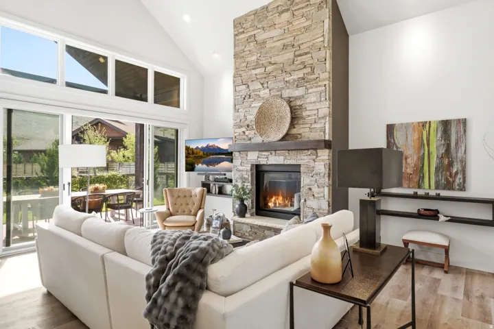 Vaulted ceiling, stone-clad fireplace with mantel, wood-finish flooring, and expansive glass sliding doors