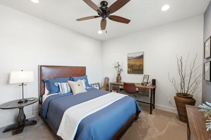 Recessed lighting, wood-finish ceiling fan, wood-finish bed frame with upholstered headboard, neutral carpet, and white walls
