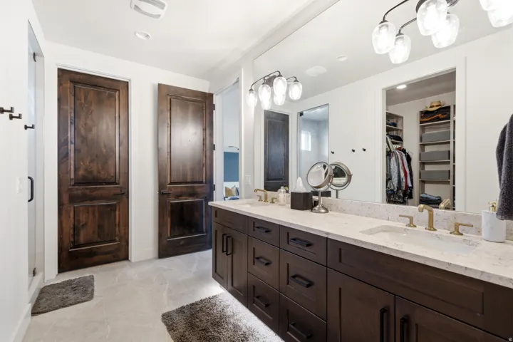 Dual vanity with dark wood-finish cabinetry, light stone countertop, and brass-finish fixtures
