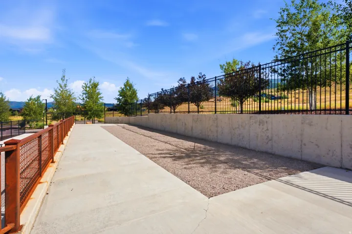 Concrete walkway with a metal mesh railing, gravel ground cover, a concrete retaining wall, and a black metal fence