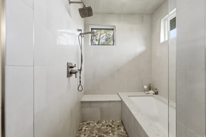 Walk-in shower with pebble tile flooring, dual shower heads, and an integrated bench