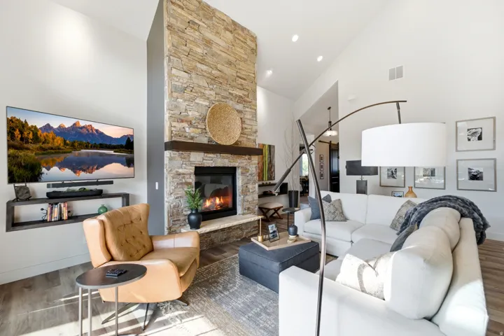 Vaulted ceiling, stone-clad fireplace with wood mantel, built-in shelving, wood-finish flooring, and recessed lighting