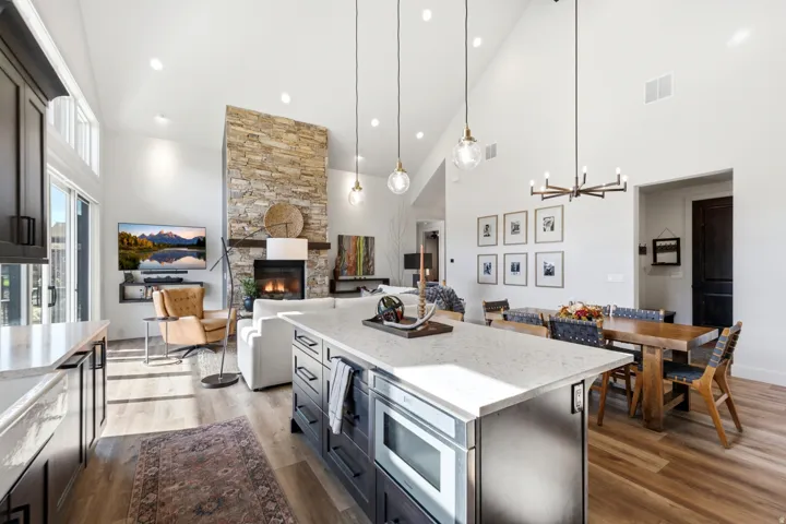 Vaulted ceilings with recessed lighting, stone-clad fireplace, wood-finish flooring, kitchen island with built-in microwave, and pendant lighting