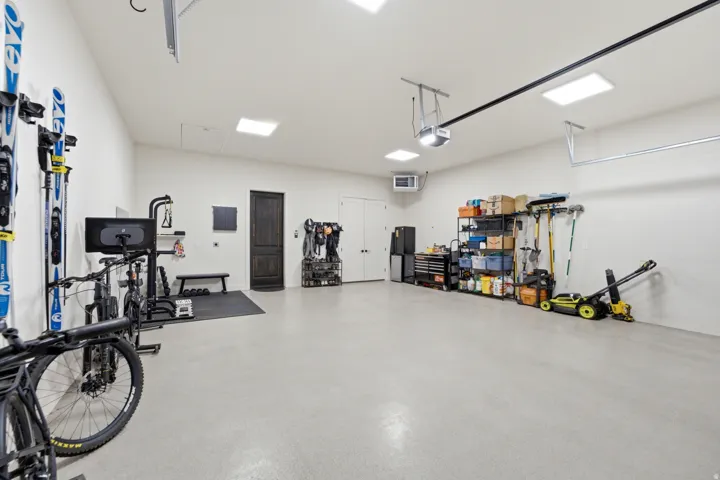 Spacious garage featuring a light-colored floor, multiple overhead light fixtures, and a dark wood-finish door