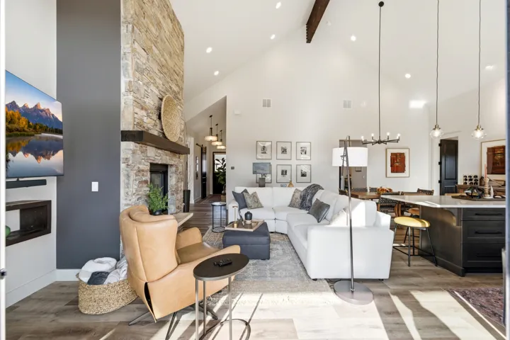 Vaulted ceilings, a stone-finish fireplace with a wood mantel, wood-finish flooring, and recessed lighting illuminate the open-concept living space