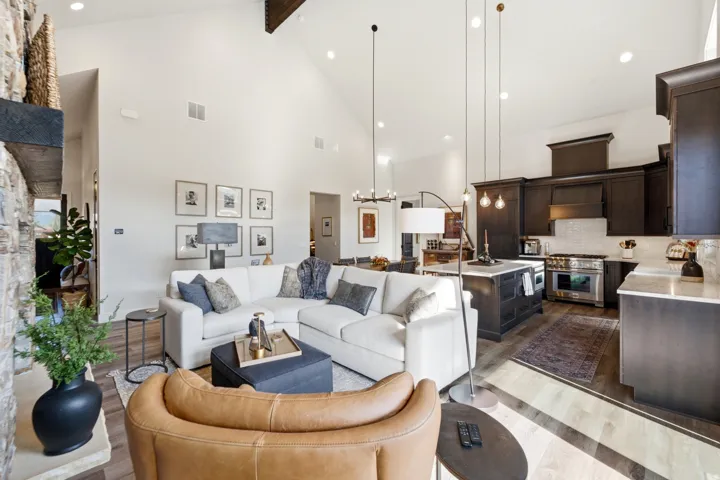 Vaulted ceilings, a stone-clad fireplace with a wood mantle, wood-finish flooring, a kitchen island with a light-toned countertop, and dark wood cabinetry