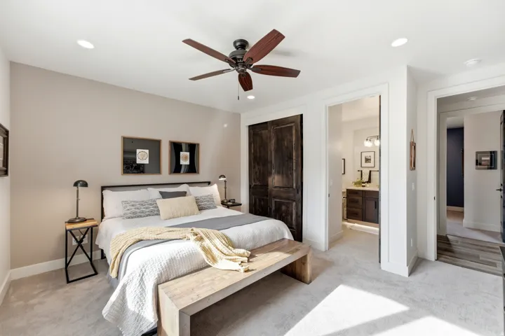 Vaulted ceiling with recessed lighting and ceiling fan, dark wood-finish barn doors, light-toned carpet flooring, and a bathroom featuring a dark wood-finish vanity