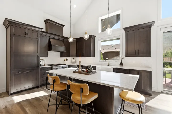 Vaulted ceilings with large windows, dark wood-finish cabinetry, white stone countertops, farmhouse sink, and wood-finish flooring