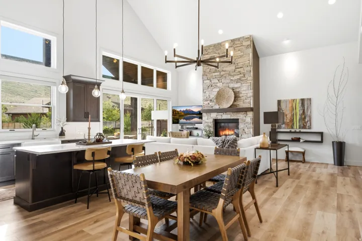Vaulted ceilings, a stone fireplace with a wood mantle, wood-finish flooring, a kitchen island with seating, and extensive window placement