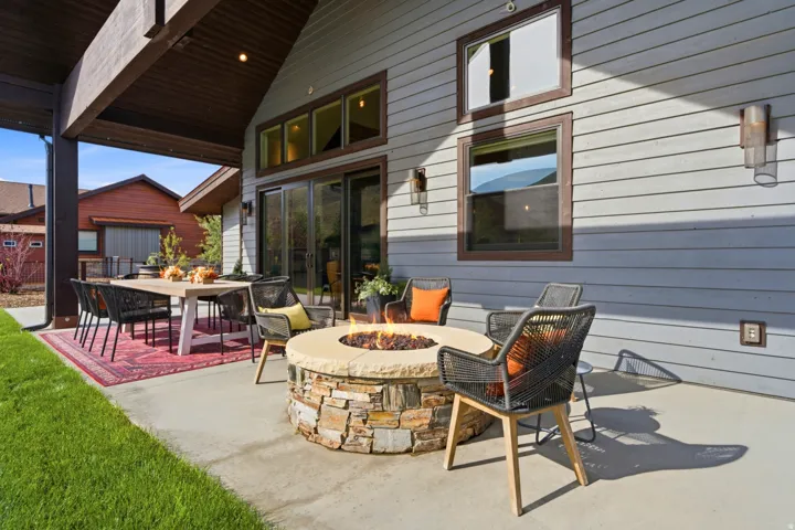 Expansive concrete patio with a stone-clad fire pit, covered outdoor dining area, and board-and-batten siding