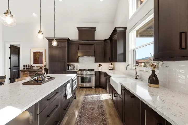 Kitchen with dark wood cabinetry, light-colored countertops, a white farmhouse sink, and stainless steel appliances