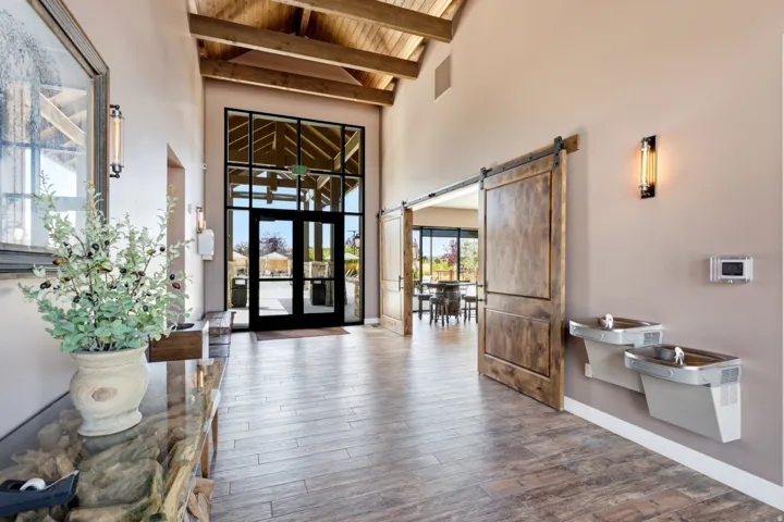 Vaulted wood-beamed ceiling, wood-finish flooring, two large sliding barn doors, a two-story glass entrance, and wall-mounted water fountains