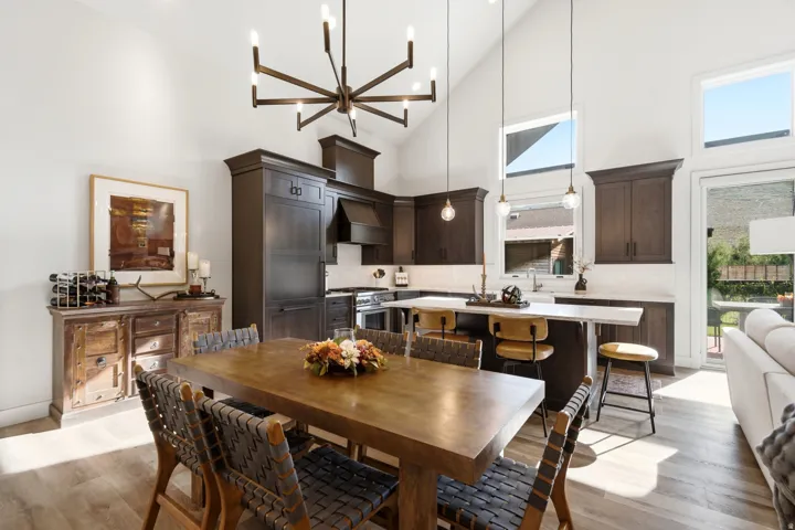 Vaulted ceiling with a chandelier, dark wood-finish cabinetry, built-in stainless steel appliances, breakfast bar with a solid surface countertop, and light wood-finish flooring