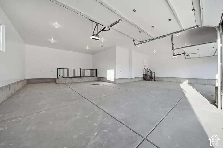 Expansive concrete flooring with a white painted ceiling, featuring recessed lighting, a raised platform with a metal railing, and an overhead garage door mechanism