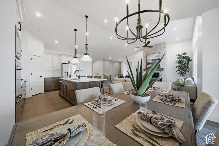 Vaulted ceilings with recessed lighting, stone-clad fireplace, wood-finish flooring, kitchen island with seating, and stainless steel appliances