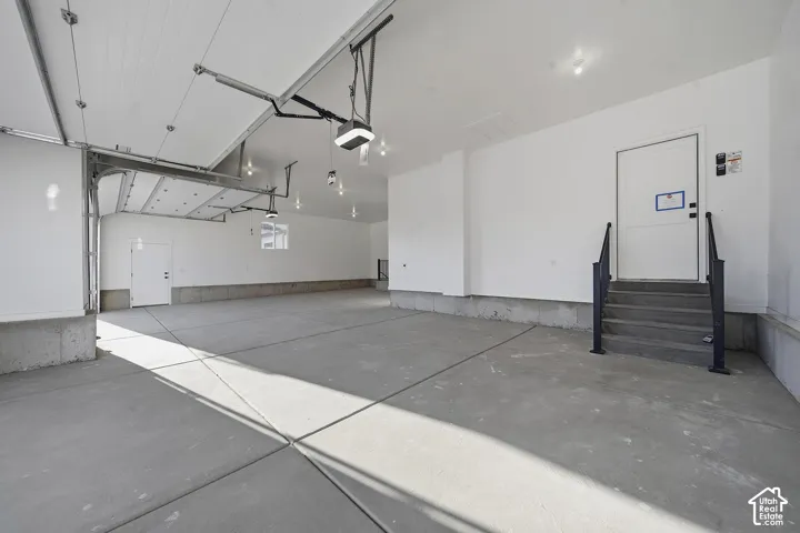 Spacious garage with multiple overhead doors, concrete flooring, recessed lighting, and a utility access door with steps and handrails