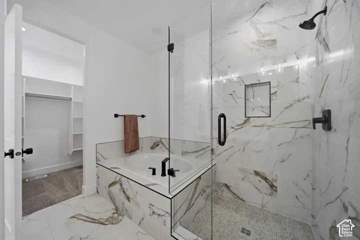 Soaking tub with matte black fixtures, glass-enclosed shower, white marble-look tile, and built-in closet shelving