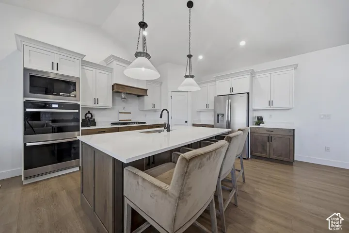 Kitchen featuring white shaker cabinetry, stainless steel appliances, a center island with countertop seating, wood-finish flooring, and pendant lighting