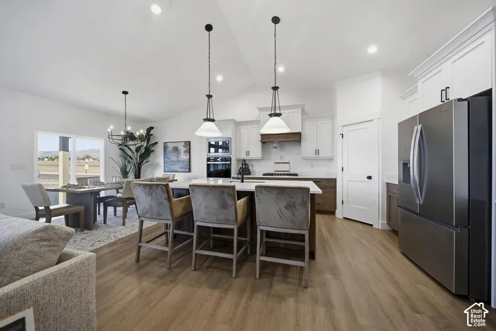 Open-concept kitchen and dining area featuring stainless steel appliances, white cabinetry, a large center island with seating, pendant lighting, wood-finish flooring, and recessed ceiling lights
