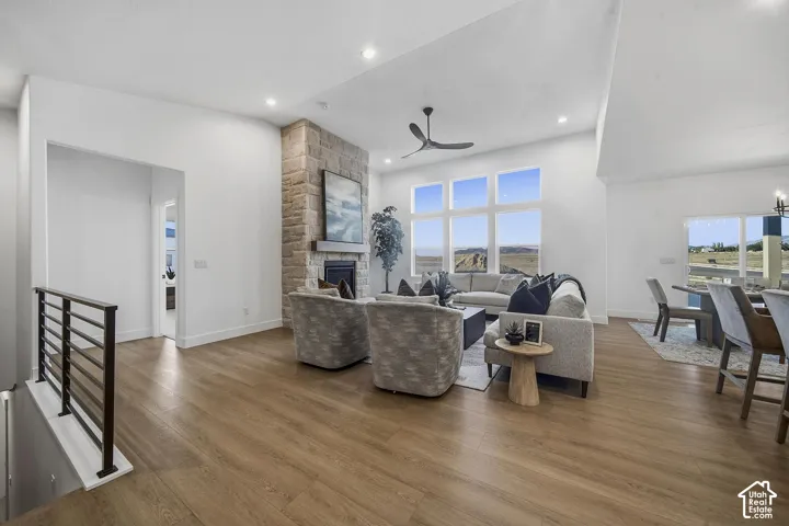 Vaulted ceiling with recessed lighting, stone-clad fireplace with mantel, large picture windows, wood-finish flooring, and open railing
