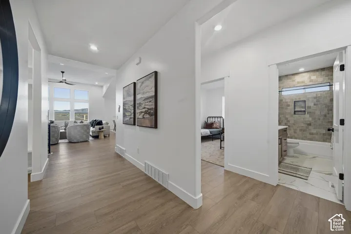 Wood-finish flooring throughout, with a spacious living area featuring large windows and a ceiling fan