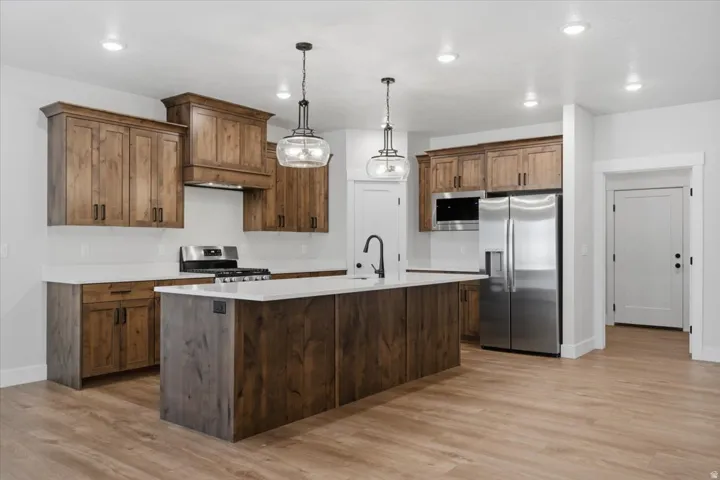 Kitchen featuring wood-finish cabinetry, stainless steel appliances, a center island with a sink, white countertops, and LVP flooring