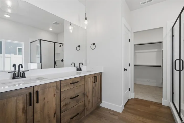 Dual vanity with a white countertop and undermount sinks, wood-finish cabinetry with matte black hardware, a frameless mirror, and wood-finish flooring
