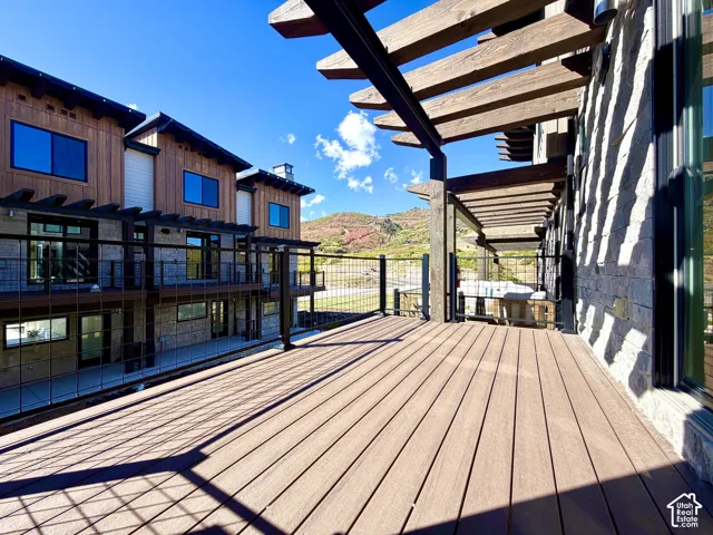 Expansive wood-finish deck with a built-in pergola, stone-clad exterior, and metal railing