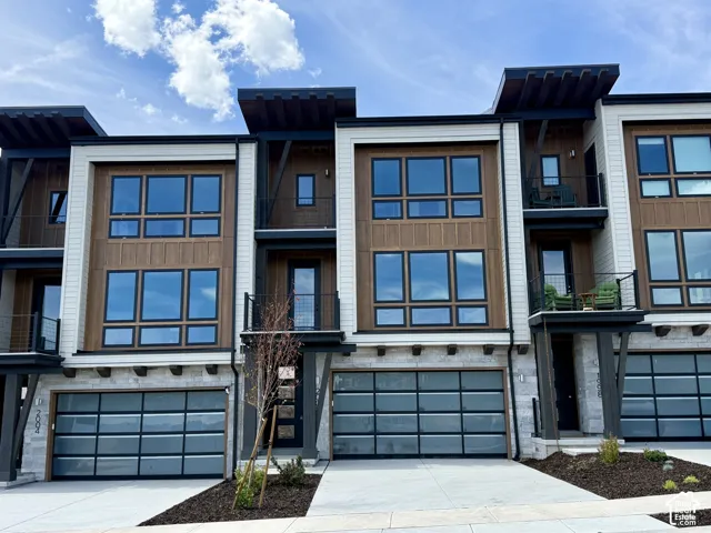 Modern townhome exterior featuring multi-panel garage doors, stone veneer, wood-tone siding, and multiple balconies with metal railings
