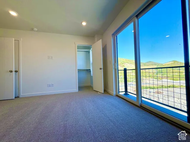 Spacious room featuring neutral carpeting, recessed ceiling lighting, a walk-in closet with shelving, and sliding glass doors leading to a balcony with a metal railing