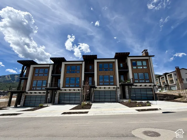 Contemporary multi-level townhome architecture featuring extensive window placements, rich wood-tone siding, and integrated two-car garages with frosted glass panels