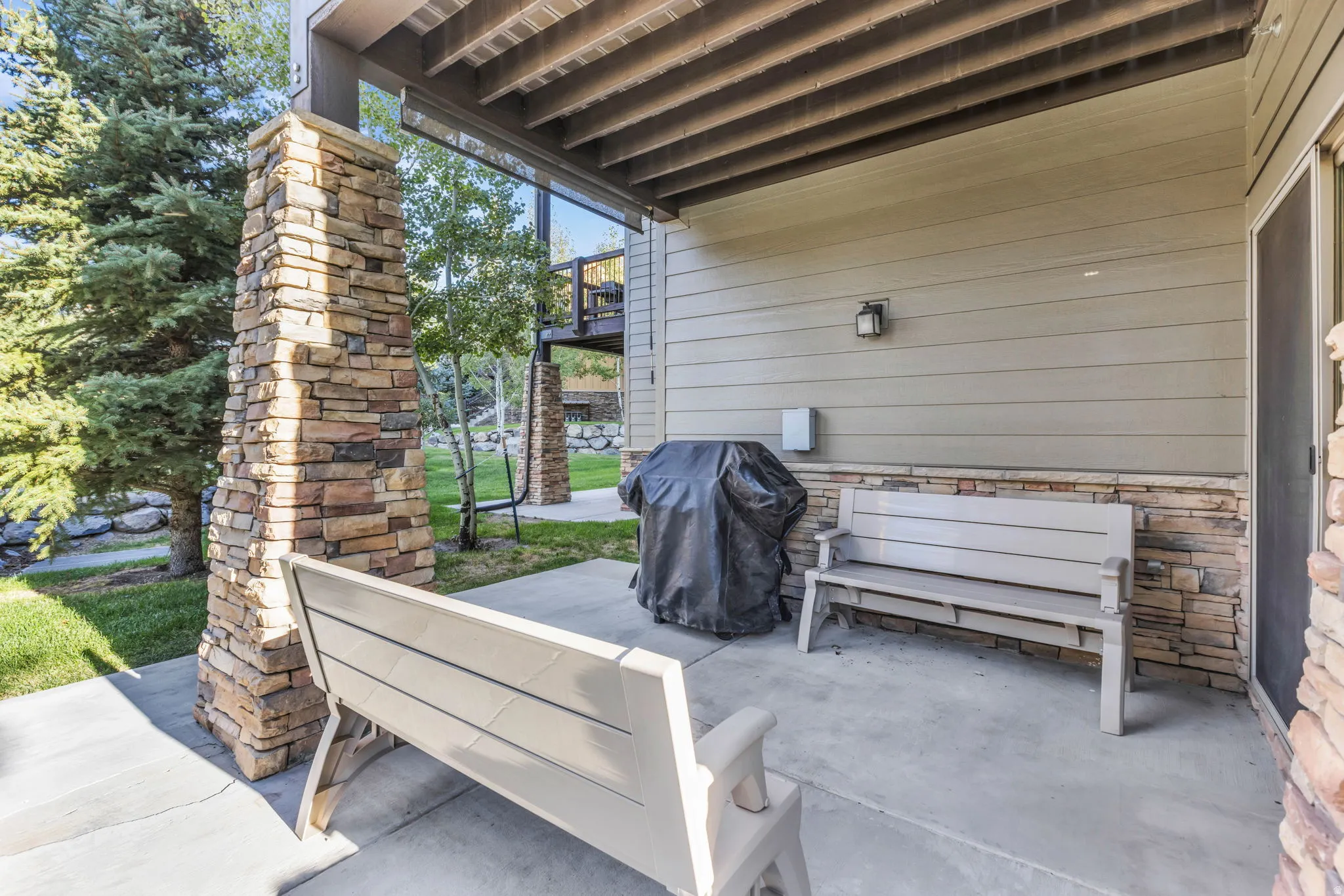 Covered patio featuring a concrete surface, stone-clad support columns, and horizontal siding