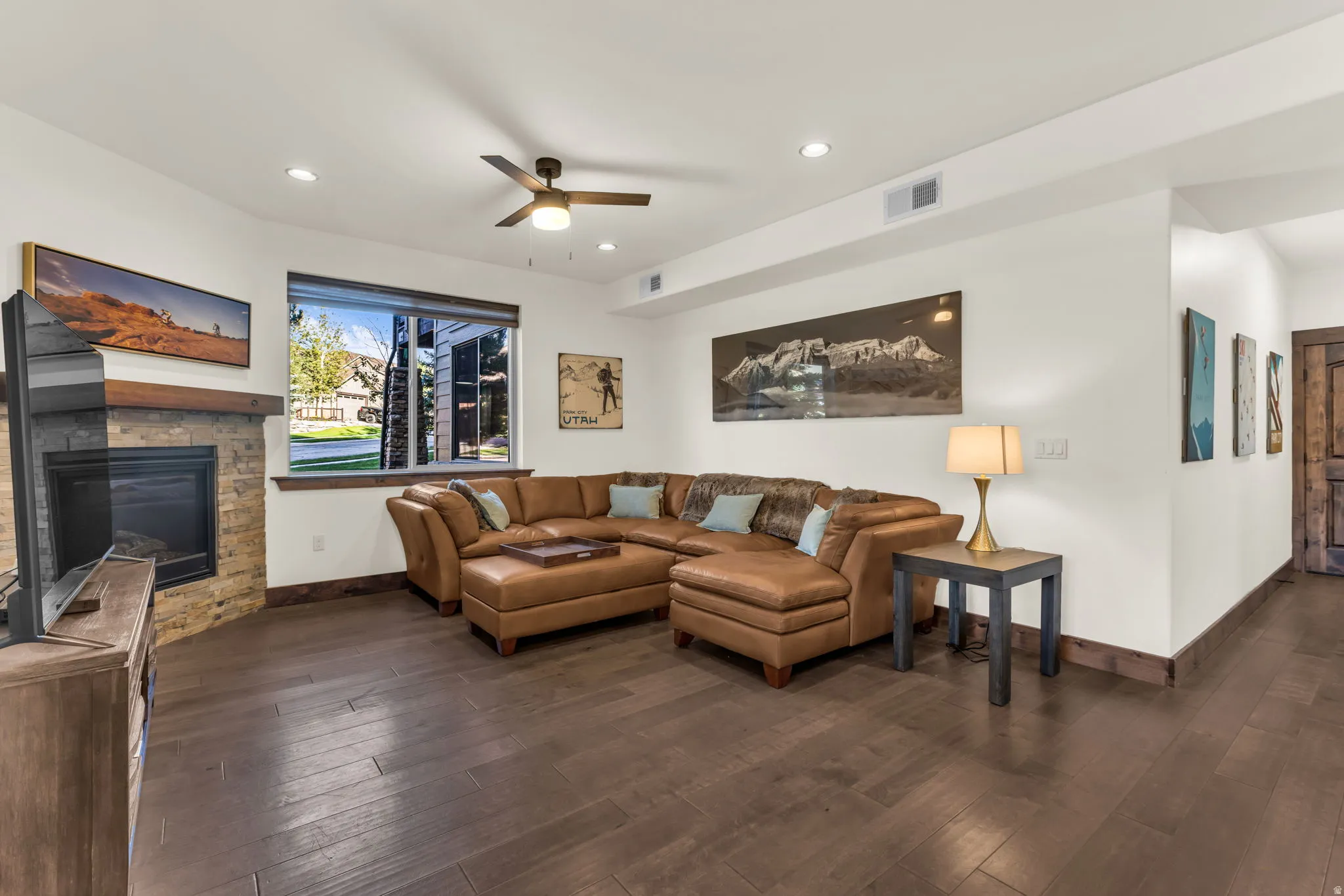Living area featuring wood-finish flooring, a stone-clad fireplace with a wood mantel, a ceiling fan, recessed lighting, and a large window