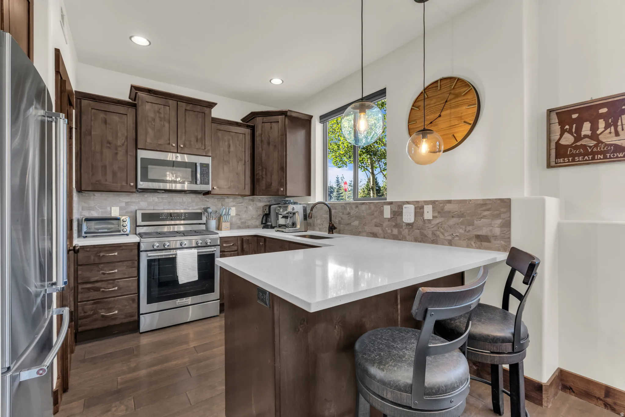 Kitchen featuring wood-finish flooring, dark wood cabinetry, stainless steel appliances, and a light-toned countertop with a stone tile backsplash