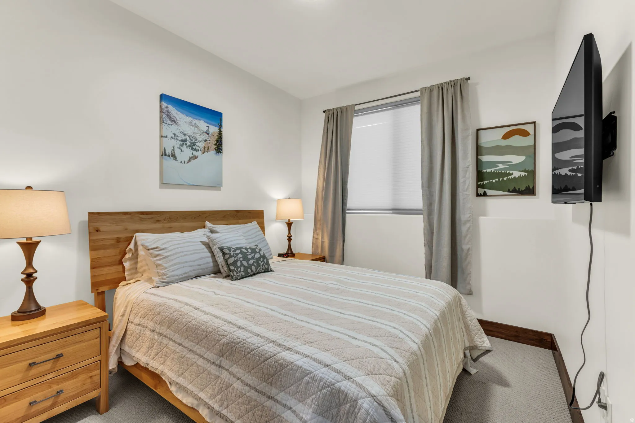 Wood-finish headboard, light gray carpet, window with blinds, baseboard trim