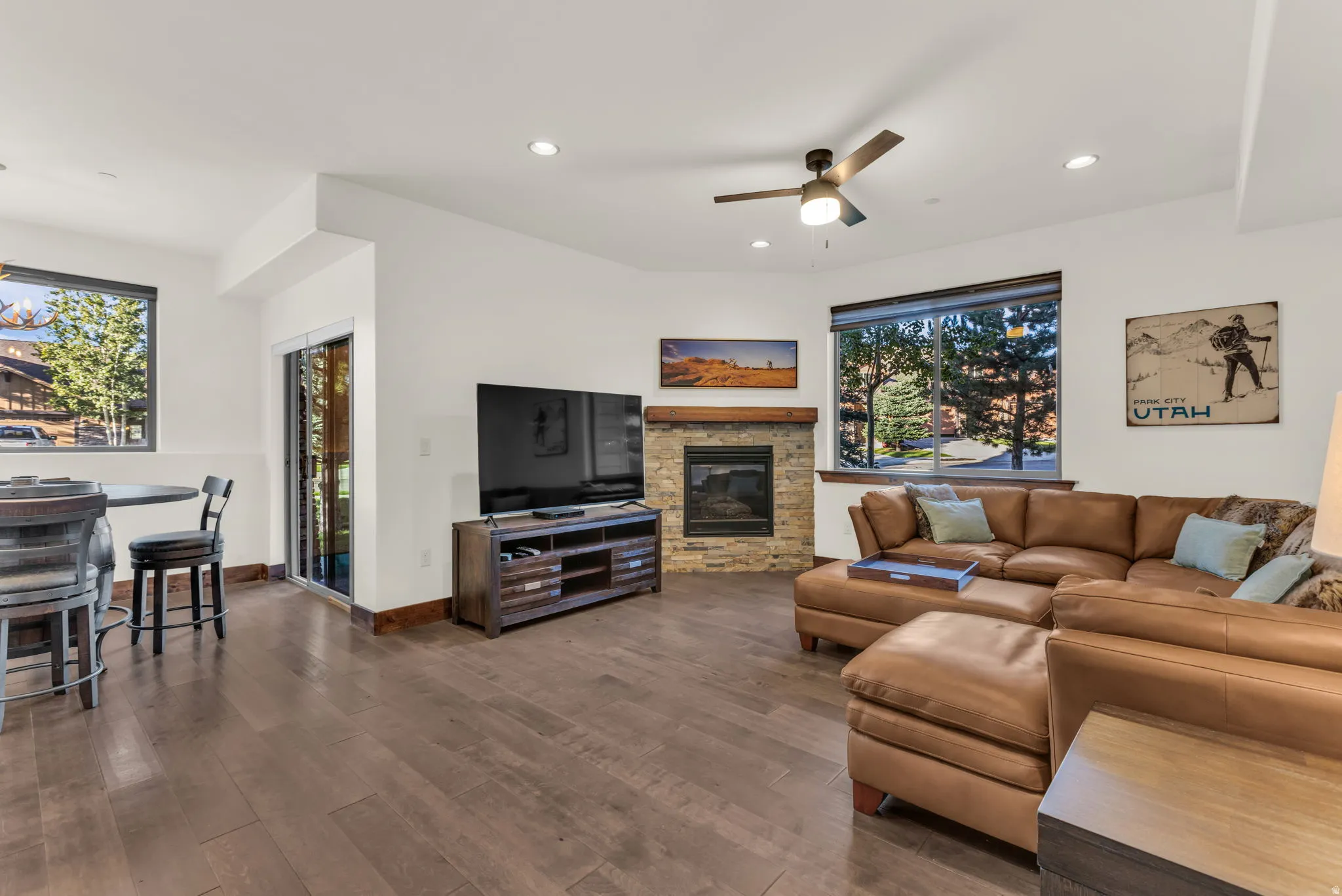 Spacious living area featuring wood-finish flooring, a stone-surround fireplace with a wood mantle, recessed lighting, and a ceiling fan
