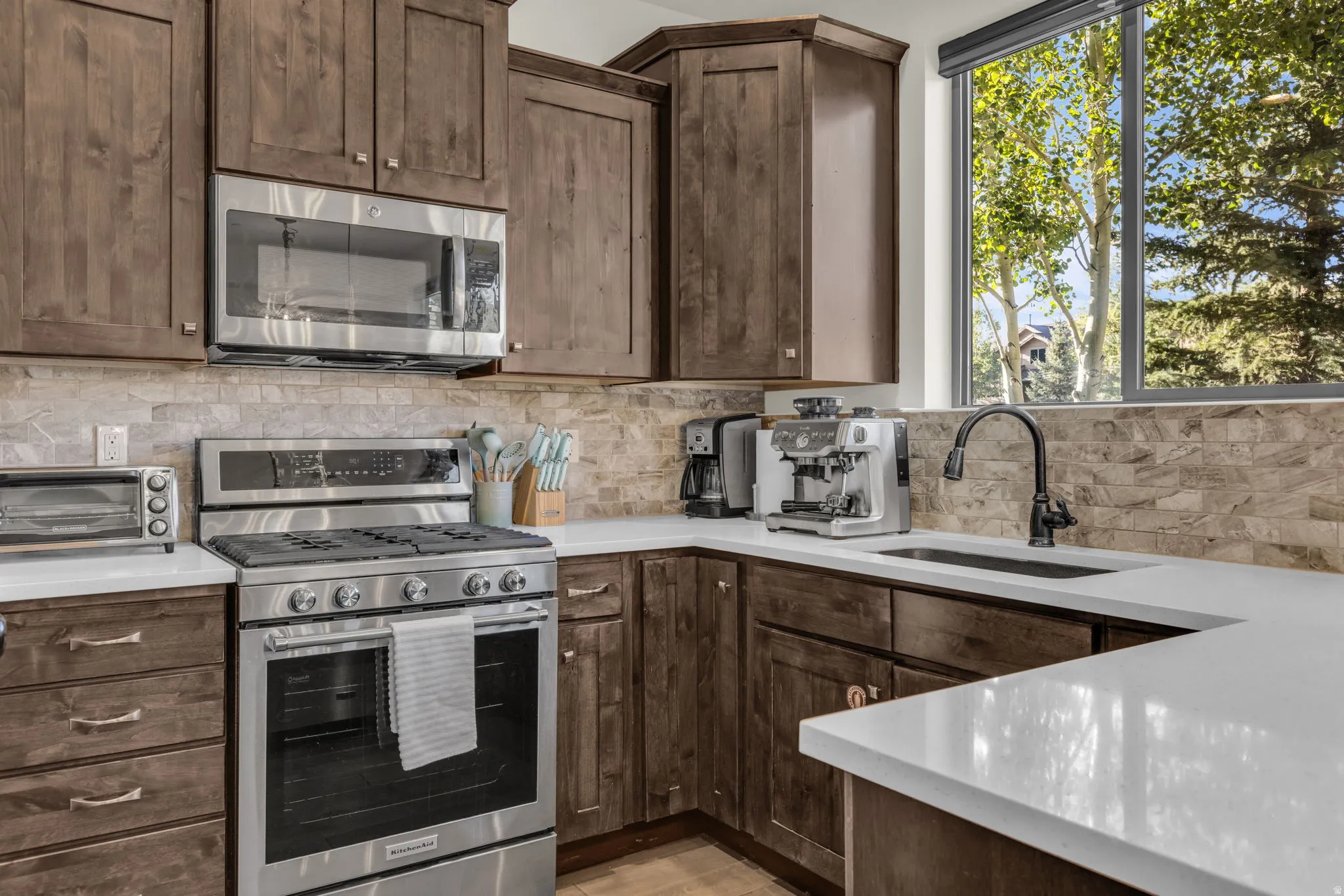 Kitchen featuring wood cabinetry, stainless steel appliances, a tile backsplash, light-toned countertops, and a window with exterior scenery