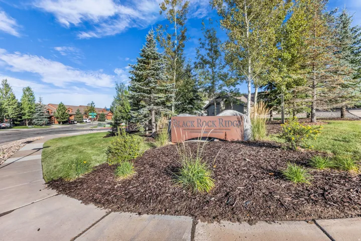 Landscaped entry featuring a stone monument sign and mature trees
