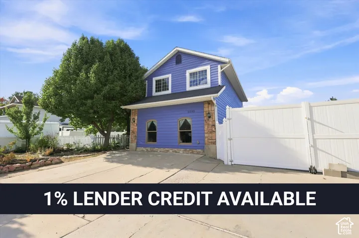 Two-story exterior featuring blue horizontal siding, stone veneer accents, arched windows, and a concrete driveway enclosed by a white privacy fence